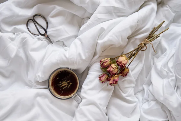 Cup of coffee, dry roses and vintage scissors on bed — Stock Photo, Image