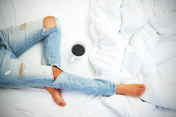 Jovem mulher desfrutando de seu café enquanto se senta na cama . — Fotografia de Stock