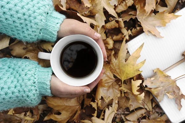 Mujer manos sosteniendo taza de café sobre las hojas de fondo . —  Fotos de Stock