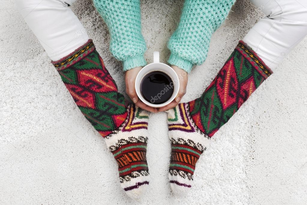 Woman hands holding cup of coffee next to her feet with socks on