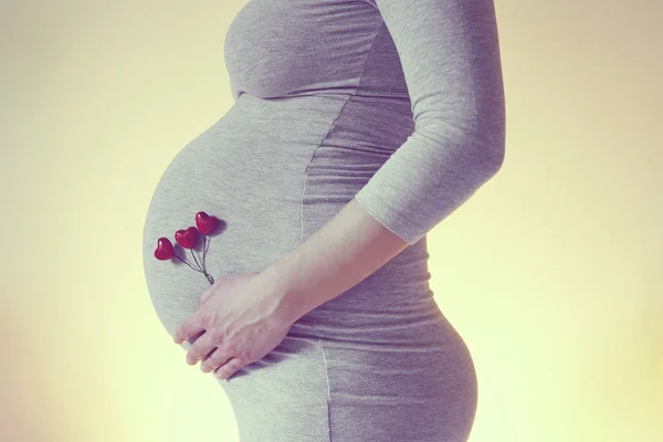 Zwangere vrouw zetten hart vorm accessoires in haar buik — Stockfoto