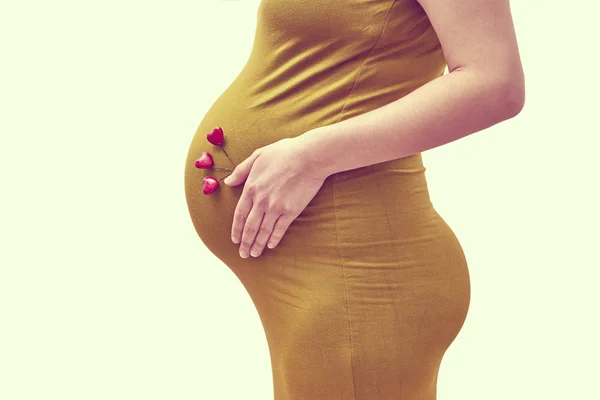 Έγκυος γυναίκα βάλει Αξεσουάρ σχήμα καρδιάς στην κοιλιά της — Φωτογραφία Αρχείου