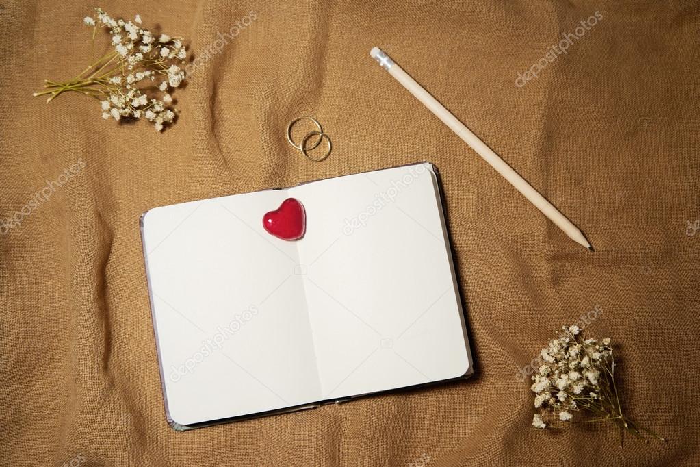 Blank notebook with heart and wedding rings on sackcloth backgro