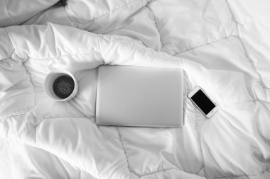 Yatak, dizüstü bilgisayar, akıllı telefon ve beyaz fincan kahve w üzerinde çalışma