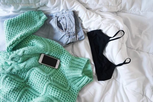 Kvinnlig outfit och smartphone läggas ut på sängen, morgonljuset — Stockfoto