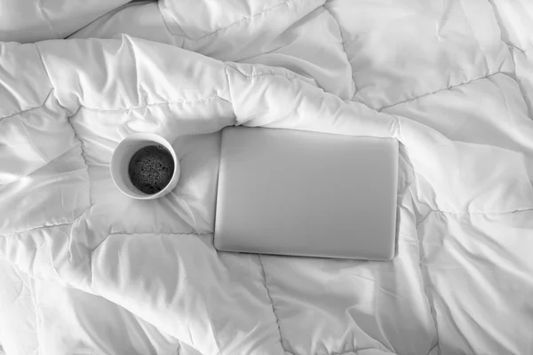 Trabajar en la cama, portátil y taza de café blanco en la cama blanca, mo — Foto de Stock