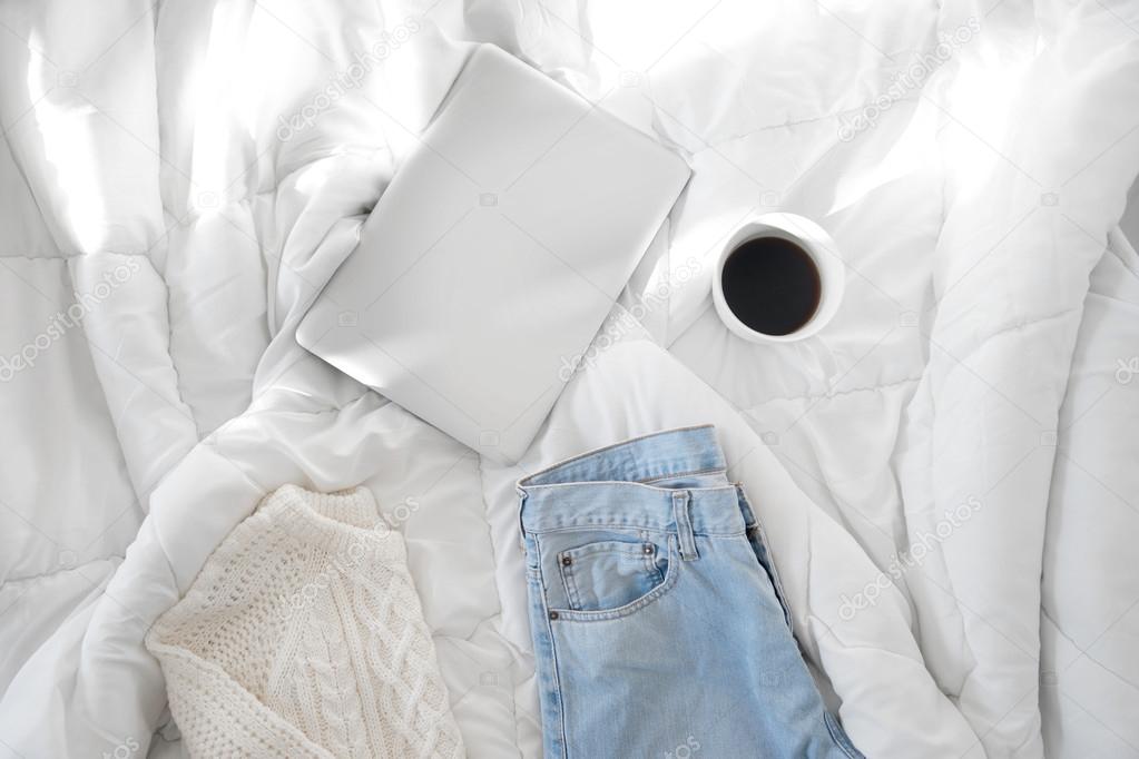 Female outfit, a  cup of coffee and a laptop laid out on bed, mo