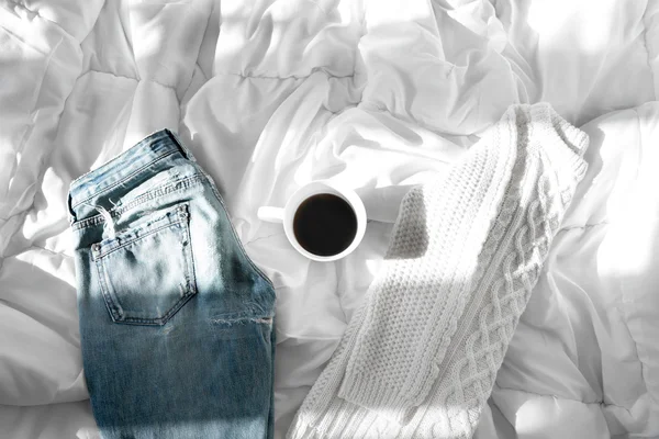 Ženské oblečení a šálek kávy rozloženy na posteli, ranní světlo — Stock fotografie