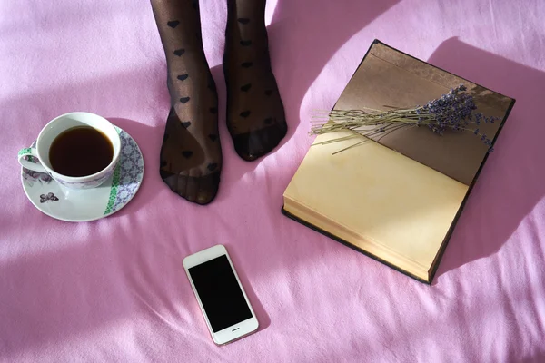 Γυναίκα στο κρεβάτι με το smartphone, το σημειωματάριο και το φλιτζάνι του καφέ — Φωτογραφία Αρχείου