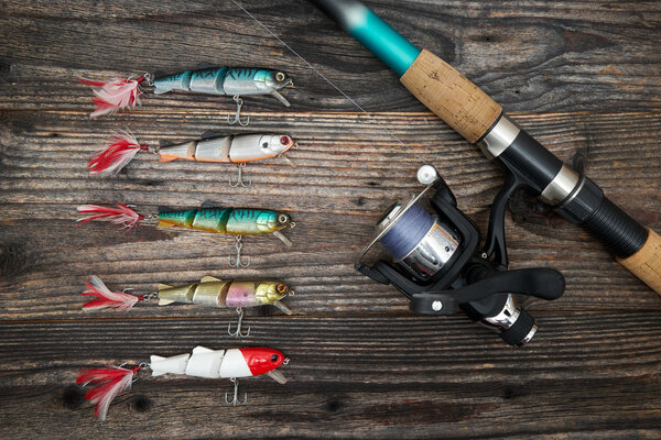 Spinning rod, reel and fishing baits isolated on wooden backgrou