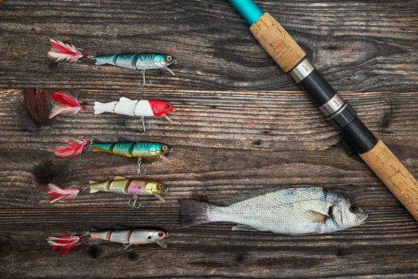 Caña giratoria, carrete y cebos de pesca aislados en el fondo de madera —  Fotos de Stock