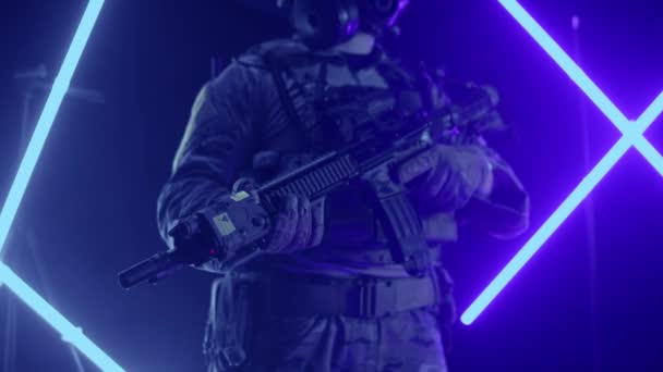 Um soldado de uniforme com uma espingarda nas mãos sobre um fundo multicolorido no estúdio. Conceito de jogo com armas e laser tag e paintball, slow mo — Vídeo de Stock