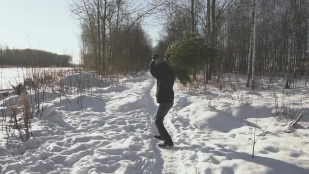 Человек в куртке веселится и танцует в лесу с рождественской елкой зимой. Концепция рождественских и новогодних каникул, медленное движение — стоковое видео