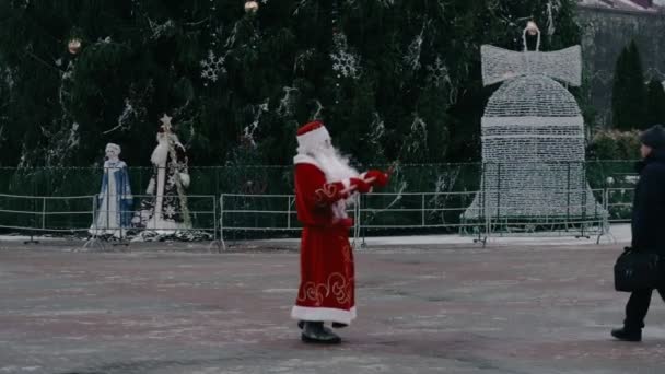 Russian Ded Moroz like a Santa Claus dances on city square near the Central Christmas tree. New year concept. Discounts and promotions, sales. Funny and comic situation — Stock Video