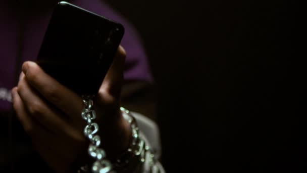 Молодий чоловік тримає смартфон у руці, до якого кріпиться ланцюжок. Поняття залежності від телефону та Інтернету в сучасному суспільстві, повільний рух — стокове відео