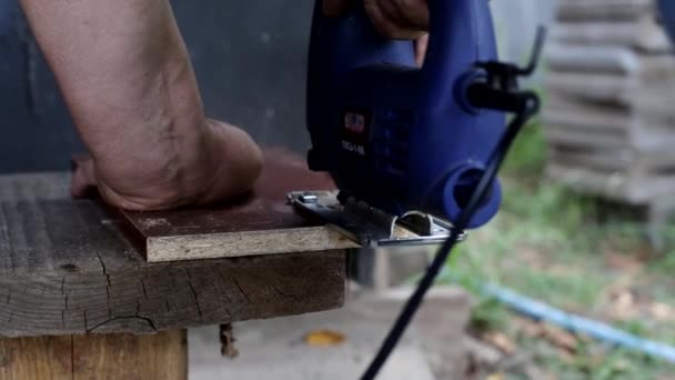 Ένας άνθρωπος κόβει ένα κομμάτι ξύλο με ένα παζλ για την κατασκευή επίπλων στη χώρα, ένα χόμπι, κοντινό πλάνο — Αρχείο Βίντεο