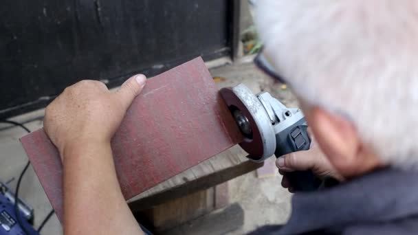 Um homem protege um painel de madeira com uma roda de moagem e um moedor. Fabricação de móveis para uma residência de verão, hobby — Vídeo de Stock