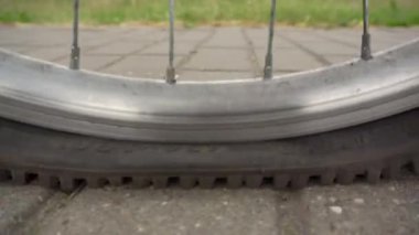 Tekerleği patlamış, lastiği patlamış bir adam bisiklet yuvarlıyor.