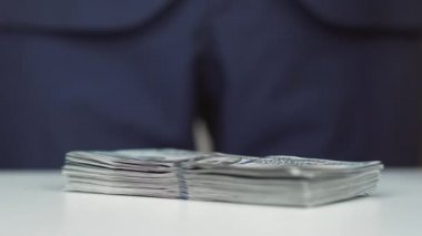 Adam masaya 100 Amerikan doları yığını para atıyor. Rüşvet, yolsuzluk konsepti. Bir bankacı ya da işadamı için başarılı bir anlaşma. 100 doların döviz değişimi.
