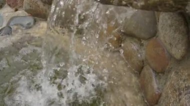 Su taşlardan gölete akar. Küçük yapay şelale, dinlenme ve meditasyon, metin için arkaplan, yavaş çekim