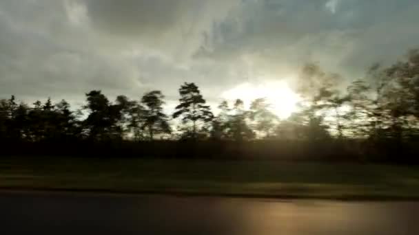 Vista desde la ventana del coche mientras conduce. El sol poniente se rompe a través de las nubes en el cielo después de la lluvia, fondo, viajes — Vídeos de Stock