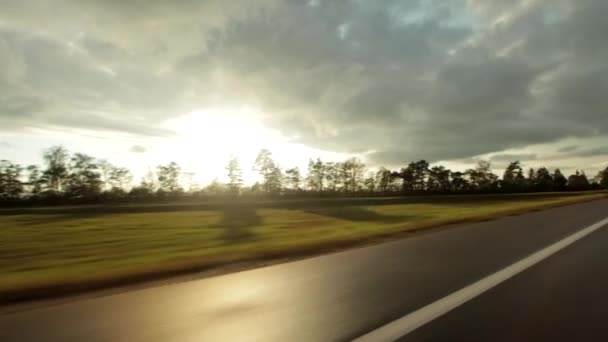 運転中に車の窓からの眺め。雨の後、ウェット高速道路は、太陽が空の雲の後ろから輝いている。車旅行のコンセプト — ストック動画