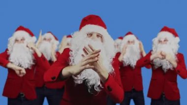 Erkekler Noel Baba dansını mavi perde arkasında sever. Noel ve Yeni Yıl konsepti. İndirim, promosyon, satış. Beyaz sakallı ve kırmızı şapkalı 7 adam Chromakey 'de.