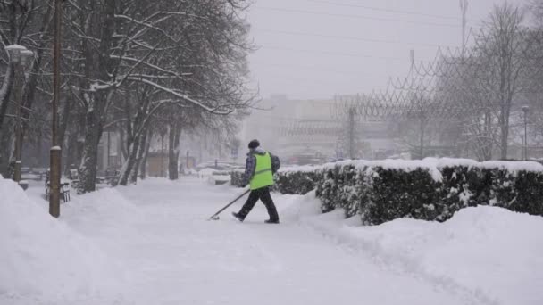 Уборщик чистит снег лопатой во время снегопада в городе, фон, замедленное движение — стоковое видео