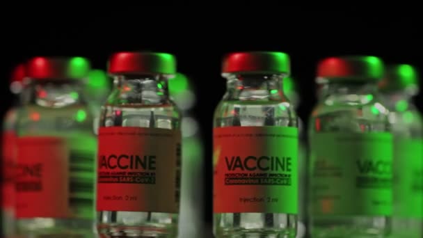 Vaccinatiekolven voor COVID-19-genezing van coronavirus worden langzaam geroteerd onder rood en groen licht. Vaccinatie, injectie, klinisch onderzoek tijdens een pandemie. Flacons, flessen draaien met de klok mee in het donker — Stockvideo