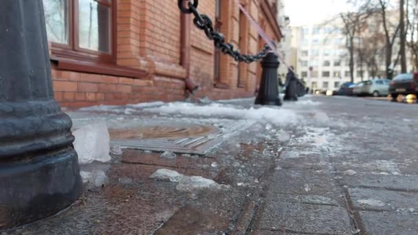 奥の屋根から降ってきた歩道には、氷やつららで濡れた雪が積もっています。都市の屋根から落下する氷による怪我のリスクの概念 — ストック動画
