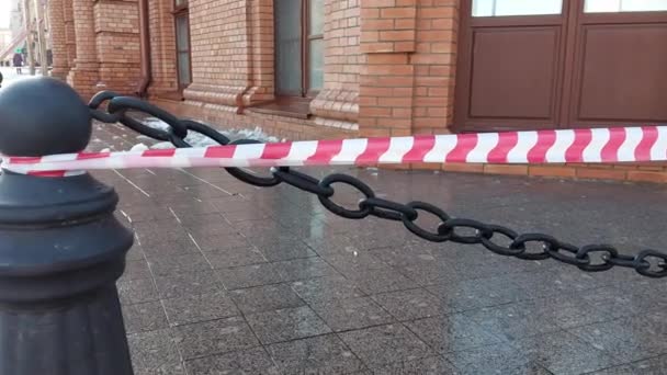 Red and white warning tape in the city near a building from the roof of which ice and icicles are falling. Risk of injury, weather — Stock Video
