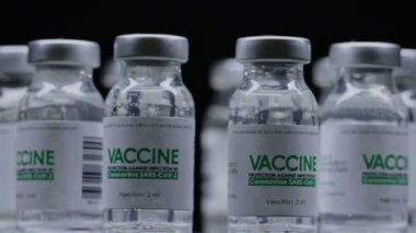 COVID-19 koronavirüs tedavisi için yapılan aşı şişeleri araştırma laboratuarında yavaşça döndürüldü. Aşı, iğne, salgın sırasında klinik deney. Şişeler, mataralar saat yönünde dönüyor. Karanlıkta geniş makro