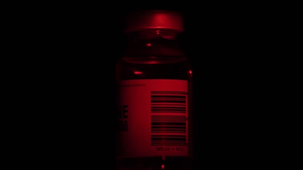 One bottle of vaccine for coronavirus COVID-19 cure are slowly spinning under a red light. Vaccination, injection, clinical trial during pandemic. Flask, vial is spinning clockwise. Macro in dark — Stock videók