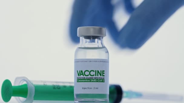 El médico toma la jeringa para inyección del frasco de la vacuna para la cura del coronavirus COVID-19 en el laboratorio de investigación. Concepto de vacunación pandémica. Macro, entrega un guante médico protector. La botella está en primer plano. — Vídeos de Stock
