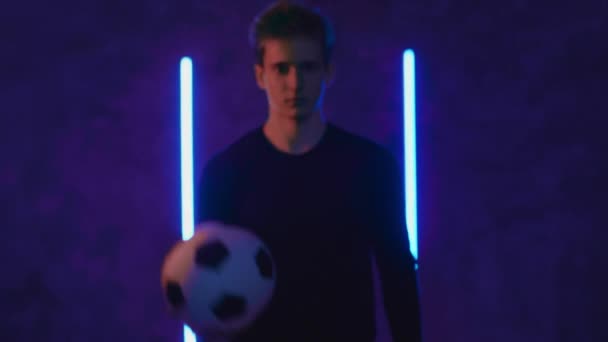Futbolcu amatör oyuncu topu karanlık bir stüdyoya atıyor. Beyaz tenli genç sporcu kameraya poz veriyor ve bakıyor. Futbol ve spor. Ağır çekimde portre. Blackmagic ProRes 'da çekildi — Stok video
