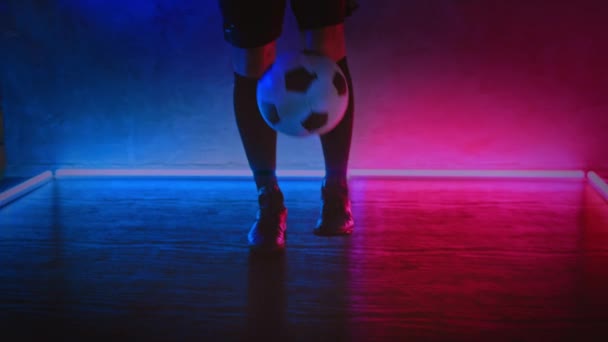 Futbolcu amatör oyuncu topa ayağıyla vuruyor. Sporcu, lacivert ışıklarla karanlık stüdyoda topu yere yuvarlıyor. Futbol sporu. Egzersiz eğitimi. Blackmagic ProRes 'da çekildi — Stok video