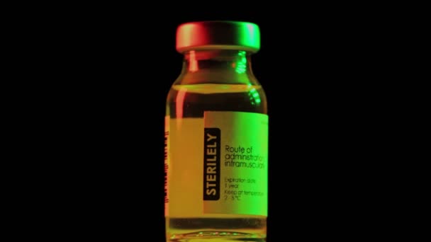 Flacon of vaccine for coronavirus COVID-19 cure are slowly spinning under red and green light. Vaccination, injection, clinical trial during pandemic. Flask, vial is spinning clockwise. Macro in dark — Stock Video