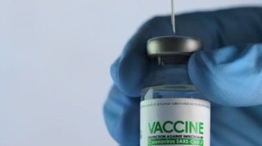 Doktor enjeksiyondan önce Coronavirus COVID-19 aşısı için aşı şişesinden şırınga dolduruyor. Aşı konsepti salgını. İğne üst kapağı delip şişenin içine giriyor. Tıbbi eldivenler. Makro yakın çekim