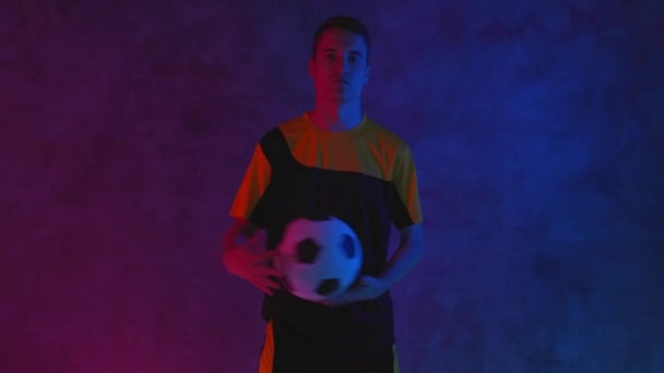 Futbolcu amatör oyuncu topu elden ele atıyor. Futbol ve spor. Karanlık stüdyoda portre. Beyaz tenli genç sporcu kameraya poz veriyor ve bakıyor. Blackmagic ProRes 'da çekildi — Stok video