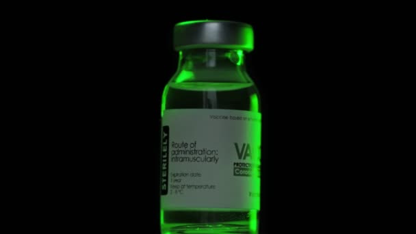Jedna butelka szczepionki przeciw koronawirusowi COVID-19 powoli obraca się pod zielonym światłem. Szczepienie, wstrzyknięcie, badanie kliniczne podczas pandemii. Flask, fiolka obraca się zgodnie z ruchem wskazówek zegara. Makro w ciemności — Wideo stockowe