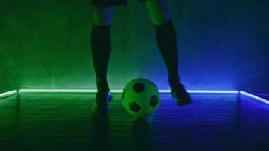 Futbolcu topu ayaktan bacağa yuvarlıyor. Futbol antrenmanı konsepti. Koyu renkli stüdyoda yeşil ışıklarla top oynayan sporcu. Spor. Blackmagic ProRes 'da çekildi. Bahis