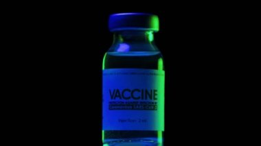 Coronavirus COVID-19 aşısı şişesi mavi ve yeşil ışık altında yavaşça dönüyor. Aşı, iğne, salgın sırasında klinik deney. Matara, şişe saat yönünde dönüyor. Karanlıktaki Macro.