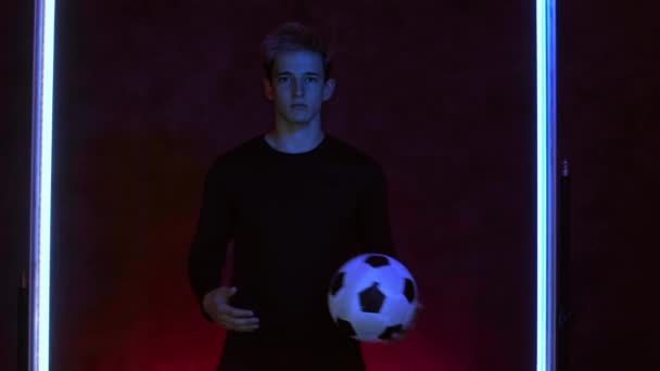 Fotboll amatör spelare kastar bollen från hand till hand. Fotboll och sport. Porträtt i mörk ateljé. Ung kaukasisk idrottsman poserar och tittar på kameran. Skjuten på Blackmagic ProRes — Stockvideo