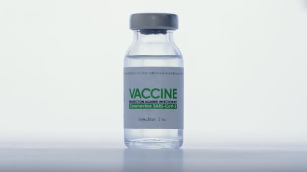 Doctor in medical glove takes vial of vaccine for injection for COVID-19 coronavirus cure in research laboratory. Vaccination concept, pandemic. Macro. Bottle flask is on white light background — Stock Video
