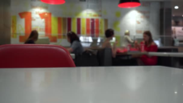 Mensen eten fastfood in restaurant of café. Ongezonde Lifestyle, gebakken en calorierijke voeding. Het risico van obesitas en overgewicht. Wazige achtergrond. Focus op stoel en tafel. Rode kleuren — Stockvideo