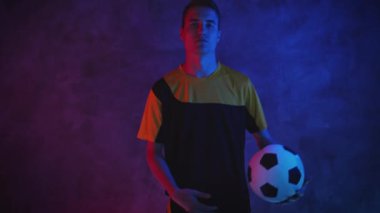 Soccer amateur player throws the ball from hand to hand. Young caucasian athlete sportsman posing and looking at the camera. Football and sport. Portrait in dark studio. Shot on Blackmagic ProRes