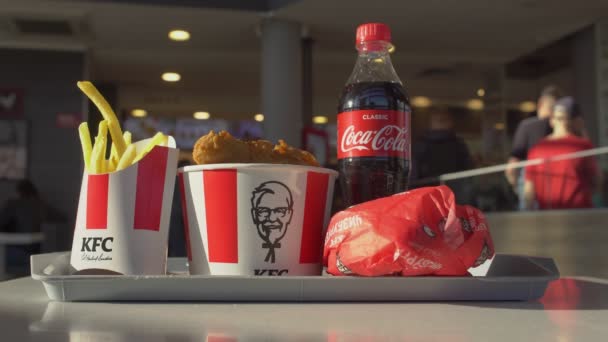MINSK, BELARUS 9.7.20: A KFC kávézó éttermében tálcán tálcán tálalják a káros gyorsételeket. Burger, szénsavas üdítőital Coca-Cola, sült krumpli, csirkeszárnyas vödör, dobverő — Stock videók
