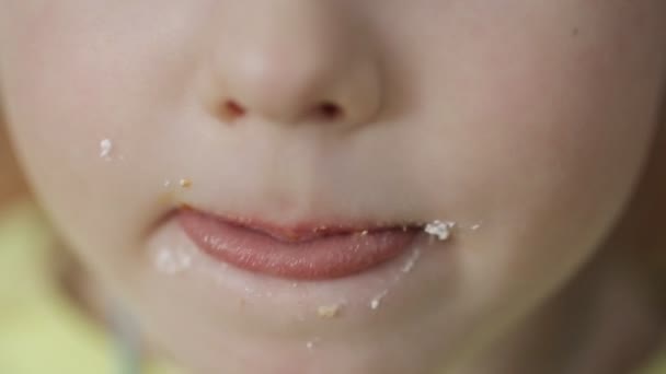 Una niña caucásica se lame los labios y la boca con la lengua después de los dulces. Niño con un diente dulce, primer plano — Vídeos de Stock