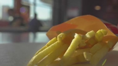 Fast food patates kızartması kafe restoranının içindeki masada yatıyor. Sağlıksız yaşam tarzı, kızarmış ve yüksek kalorili zararlı yiyecekler. Ziyaretçiler arka planda yer. Fastfood. Yakın çekim el kamerası.