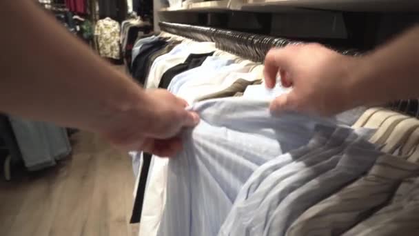 En man väljer fashionabla kläder, jackor, skjortor och T-shirts i butiken. Bakgrund, närbild, inköp — Stockvideo